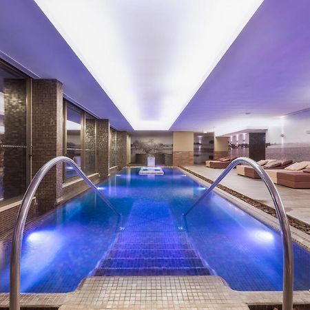 Ap Lago Montargil - Conference & Spa المظهر الخارجي الصورة The photo shows a modern indoor swimming pool area. The pool features a sleek design with steps leading into the water and a gentle curve at the sides. The water is illuminated in a blue hue, enhancing the relaxing atmosphere. Surrounding the pool ar