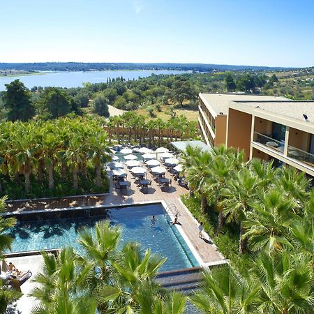 Ap Lago Montargil - Conference & Spa المظهر الخارجي الصورة The photo shows a scenic view of a modern hotel or resort. In the foreground, there is a swimming pool surrounded by palm trees, with lounge chairs positioned beside it. Sun umbrellas provide shade over the chairs. The background features a lush land