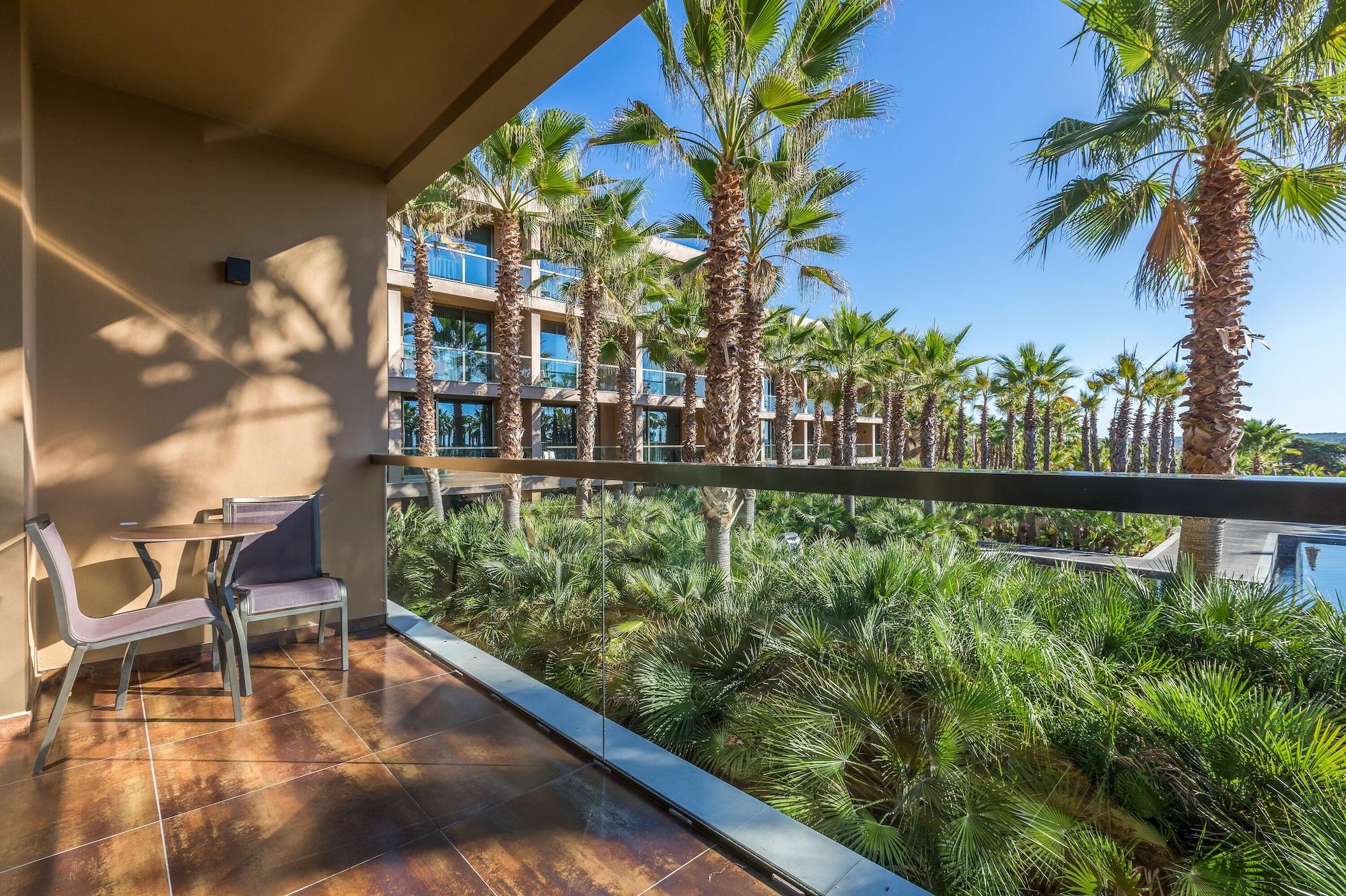 Ap Lago Montargil - Conference & Spa المظهر الخارجي الصورة The photo shows a balcony with modern furniture, including a chair and a small table. In the background, there are tall palm trees and lush greenery, suggesting a tropical or resort-like setting. The buildings in the distance are likely part of a hot
