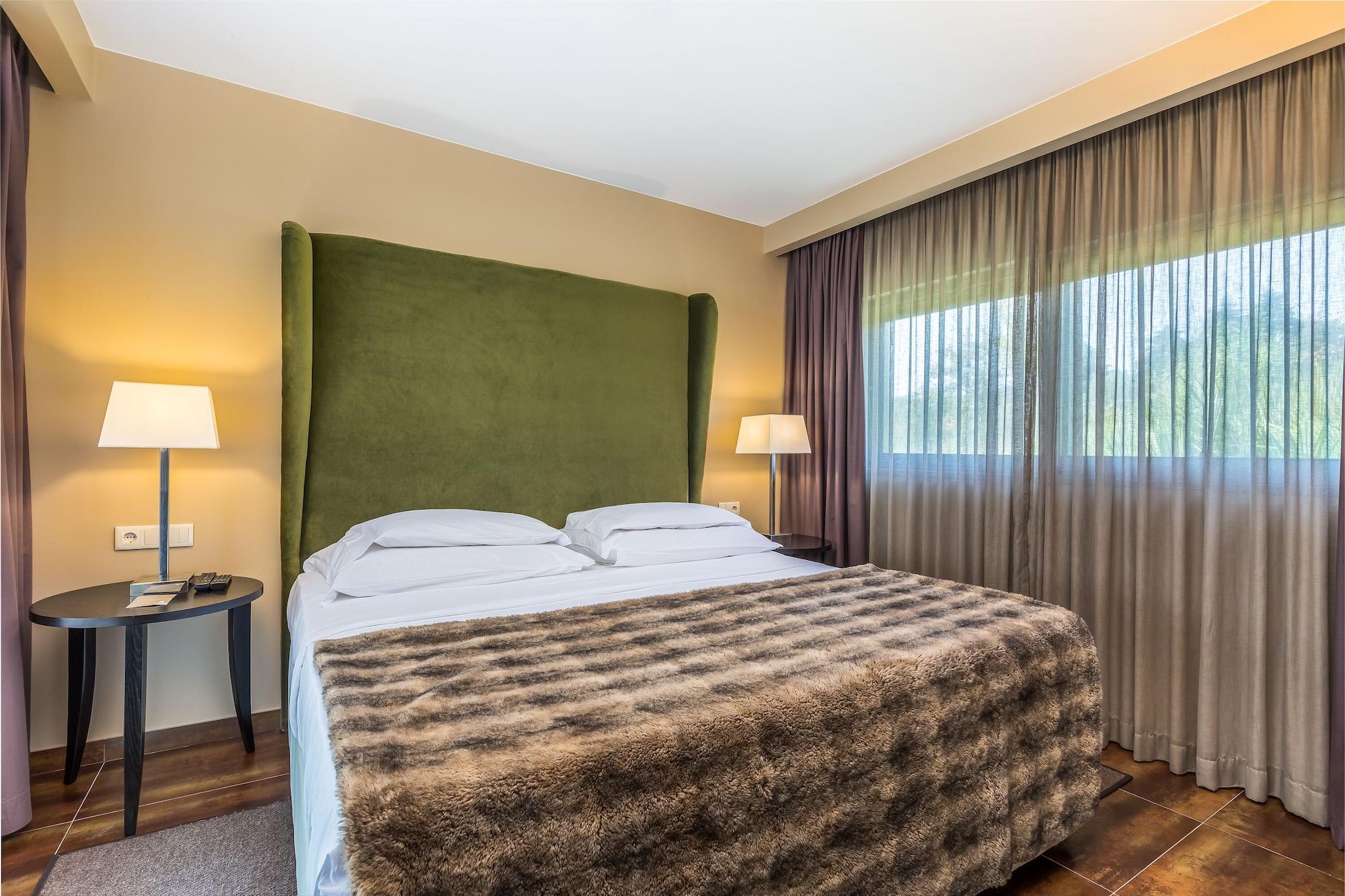 Ap Lago Montargil - Conference & Spa المظهر الخارجي الصورة The photo shows a cozy hotel room featuring a large bed with two white pillows and a fur-style blanket draped over it. Behind the bed is a tall, green headboard that adds a touch of color to the room. On either side of the bed are bedside tables, eac