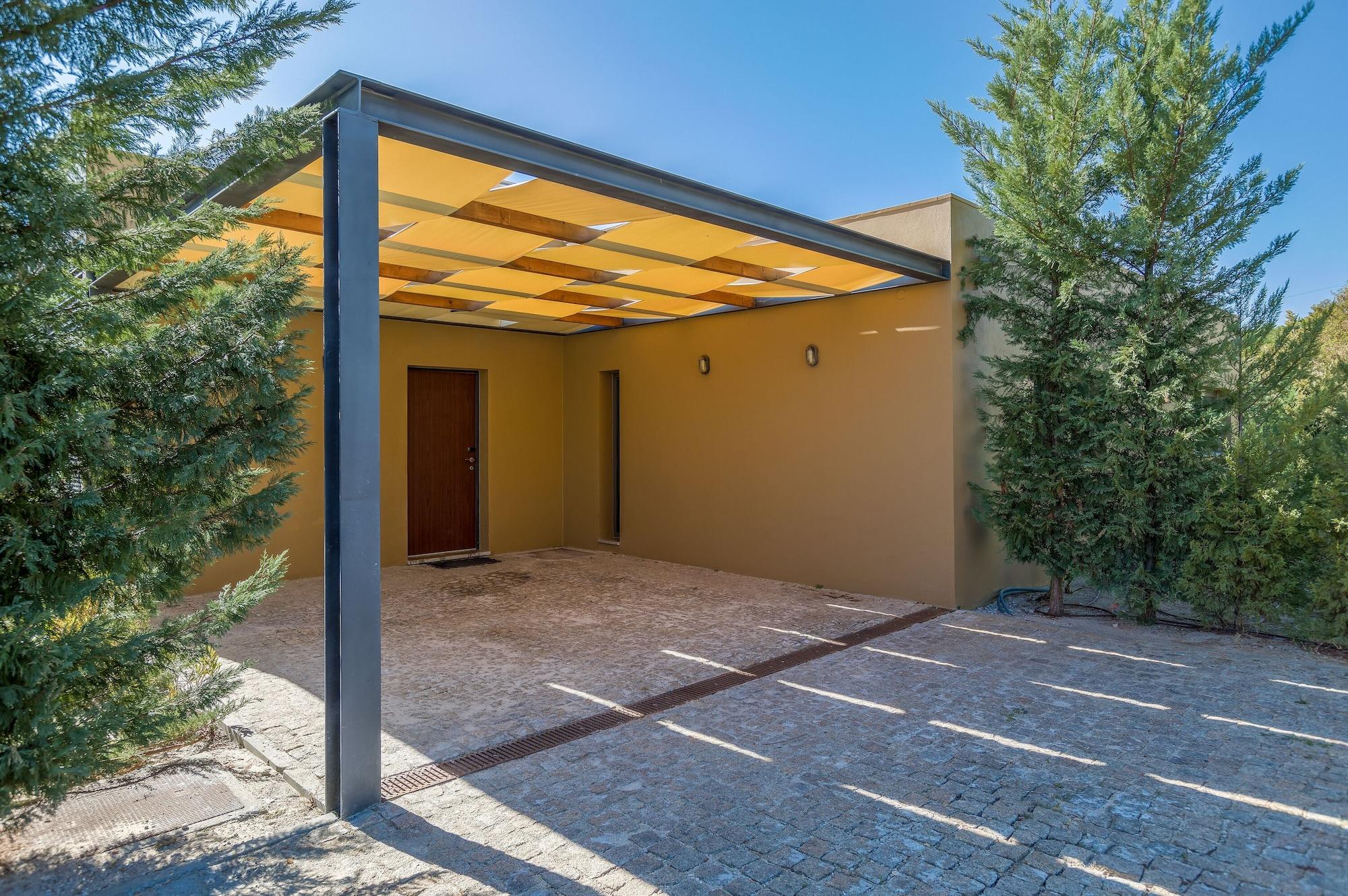 Ap Lago Montargil - Conference & Spa المظهر الخارجي الصورة The photo shows an exterior view of a modern structure with a carport. The carport has a sleek, metallic frame and a yellowish canopy above it. In front of the structure, there is a paved area made of stone or tiles. The main entrance features a wood