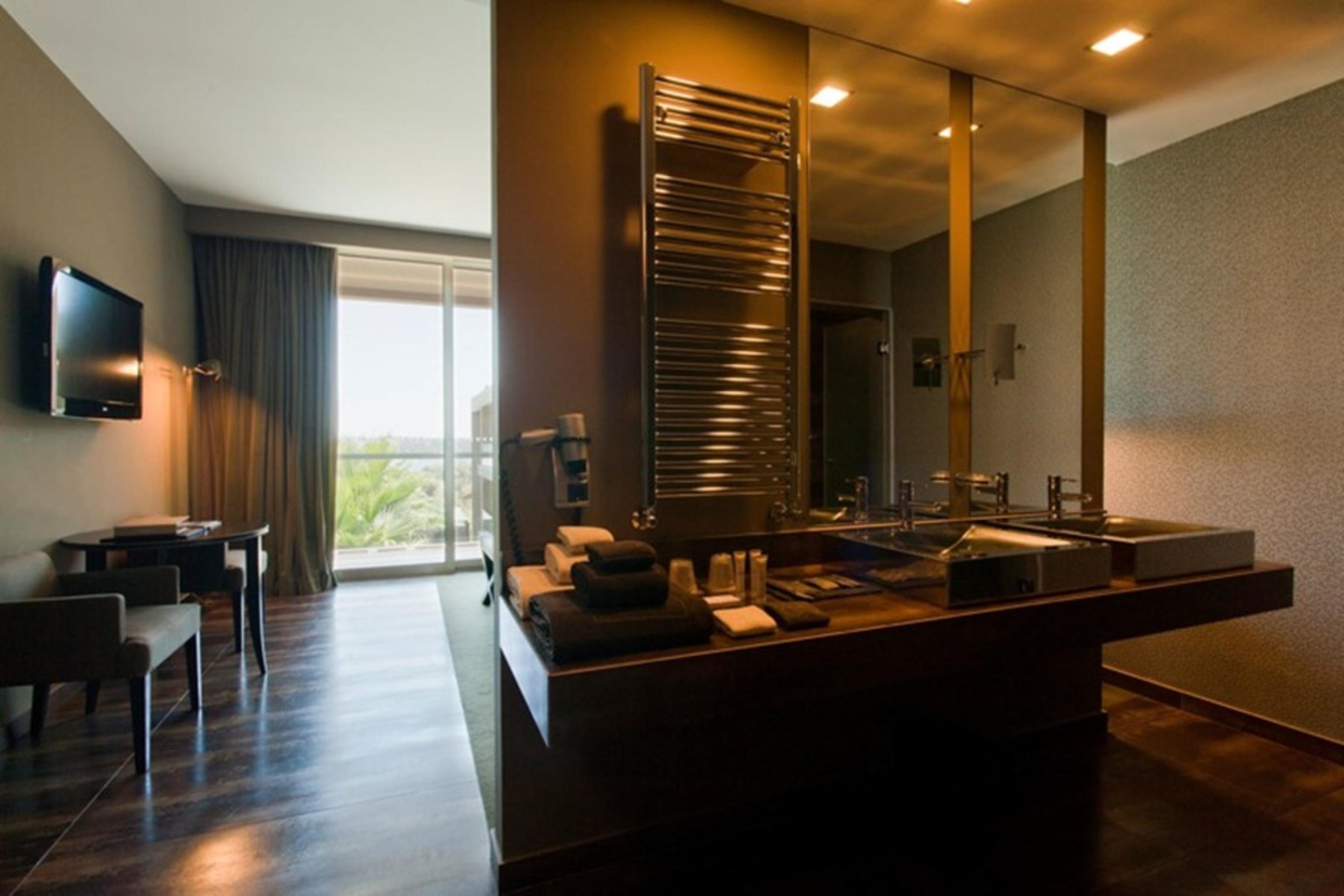 Ap Lago Montargil - Conference & Spa المظهر الخارجي الصورة The photo displays a modern hotel room with a contemporary design. The room features a large window, allowing natural light to enter and offering a view outside. On one side, there is a sitting area with a small table and chairs. The other side showc
