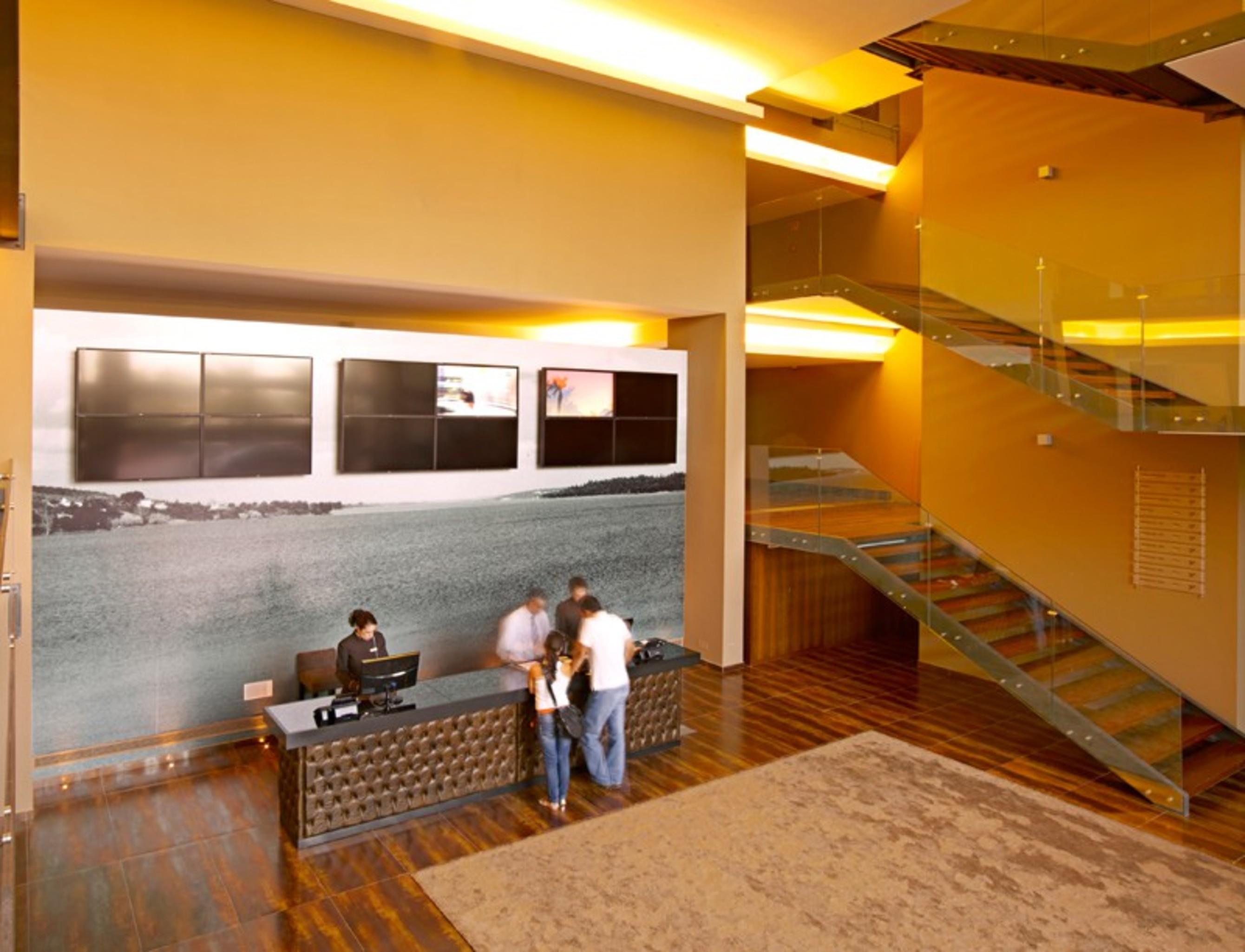 Ap Lago Montargil - Conference & Spa المظهر الخارجي الصورة The photo depicts a modern lobby area with a reception desk. The design features a combination of warm colors and wood flooring. In the background, there is a large wall-mounted screen or display, showcasing several monitors. The wall behind the desk