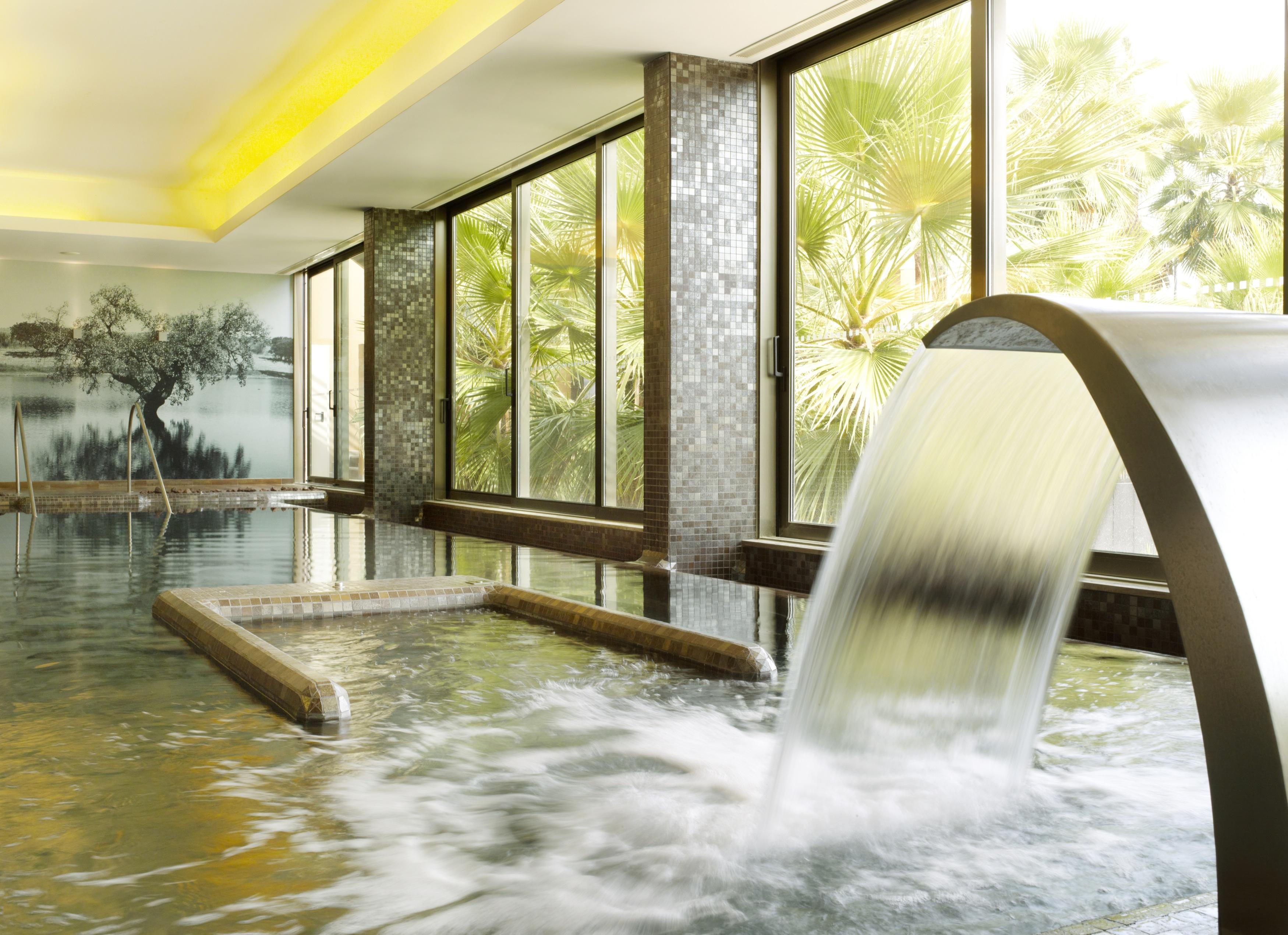 Ap Lago Montargil - Conference & Spa المظهر الخارجي الصورة The photo depicts a serene spa environment featuring a tranquil indoor pool area. There is a sleek, modern water feature that spills water gracefully into the pool. Large windows allow natural light to flood the space, showcasing views of lush greene