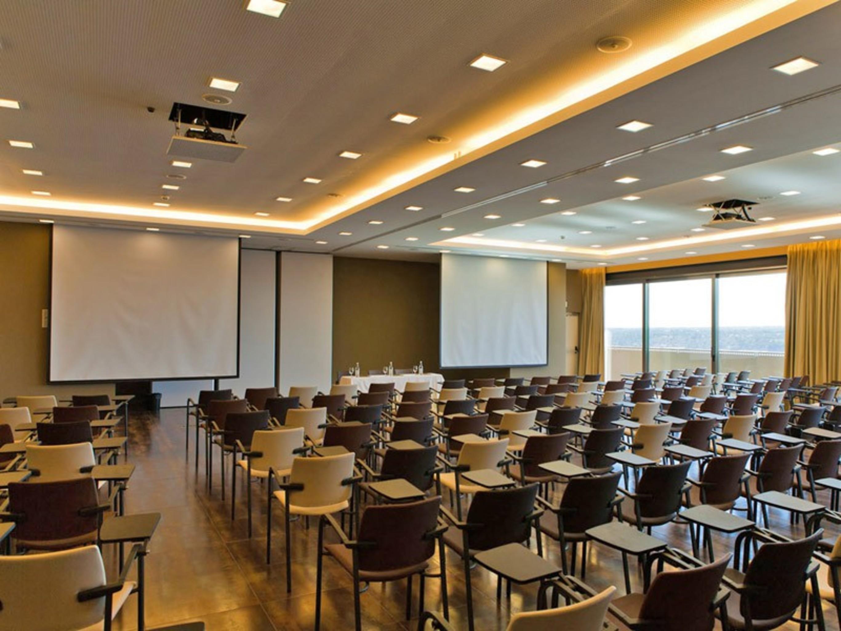 Ap Lago Montargil - Conference & Spa المظهر الخارجي الصورة The photo shows a large conference room set up for a presentation or meeting. There are multiple rows of chairs arranged in a semi-theater style, facing two large projection screens. The room has a modern design, with soft lighting and large windows 
