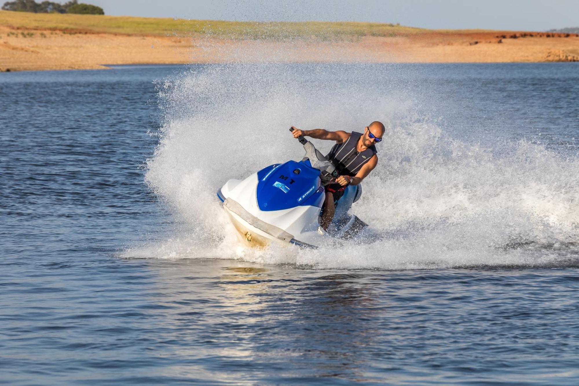 Ap Lago Montargil - Conference & Spa المظهر الخارجي الصورة The photo shows a person riding a jet ski over a body of water. The rider is wearing sunglasses and a life vest, leaning forward as the jet ski accelerates, creating a spray of water around them. The background features a natural landscape, likely a 